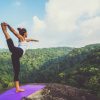 women holding yoga pose on mountains above forest