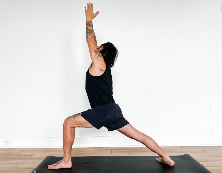 Patrick in warrior 1 pose on a yoga mat