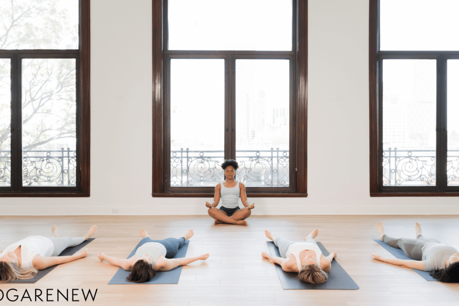 Yoga teacher sitting in front of a class in Sukasana while the students lie down in Savasana