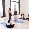 A yoga teacher in the front of the room talking through someone in headstand while 3 other students watch