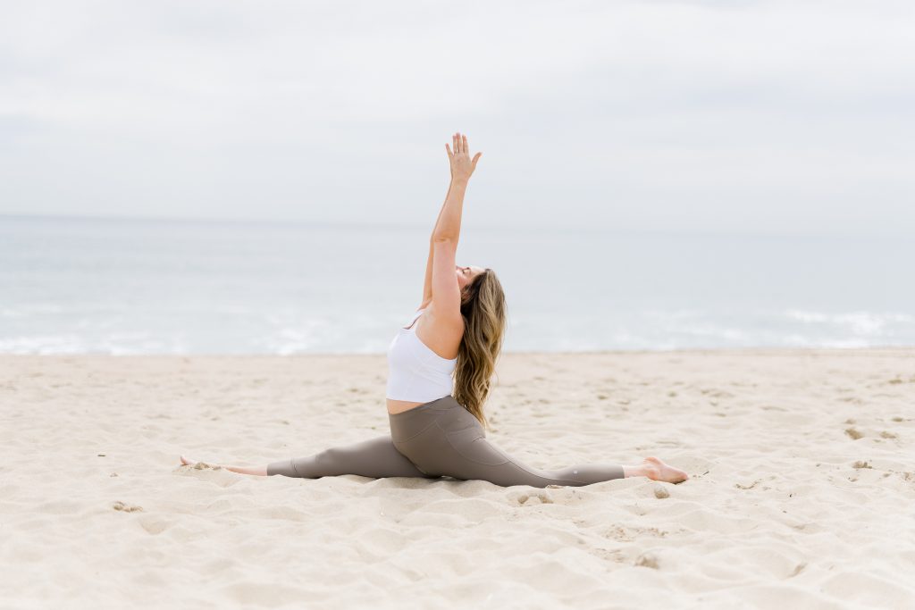 Kate Lombardo surrending to the divine in the sand on a NJ beach with her arms up overhead bringing her palms together.