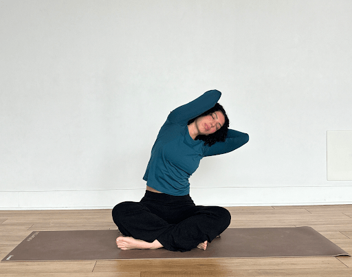 A person sitting with their elbows bent and hands behind their head doing neck rolls