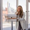 Header image of Kate Lombardo in front of a laptop in a city building resting her chin on her fist for the article: How to create a viral content plan for your wellness business