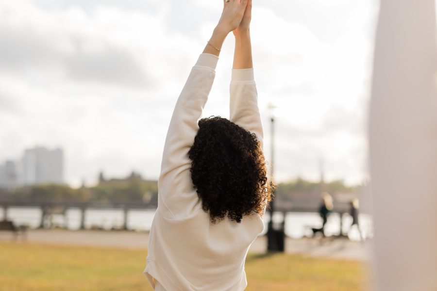 Mindful morning yoga flow image of a yogi in Urdhva Hastasana with their back towards us, overlooking a Hoboken park