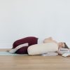 yogi resting in a restorative yoga posture with a blanket between the legs, lying on the side of the body, hugging a bolster with a blanket under the head